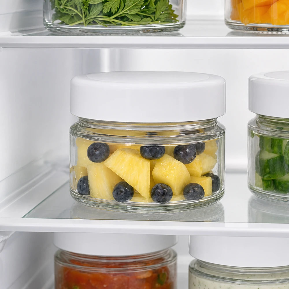 80ml Verre rond avec couvercle BasicSeal blanc UNiTWIST Un bocal rond de 80 ml au réfrigérateur contenant de l'ananas et des myrtilles montre les propriétés de conservation optimales du couvercle BasicSeal