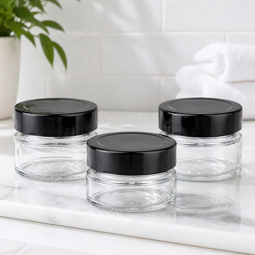 Trois pots ronds de 80ml avec couvercles noirs BasicSeal UNiTWIST sur plaque de marbre blanc Salle de bains Ambiente vide