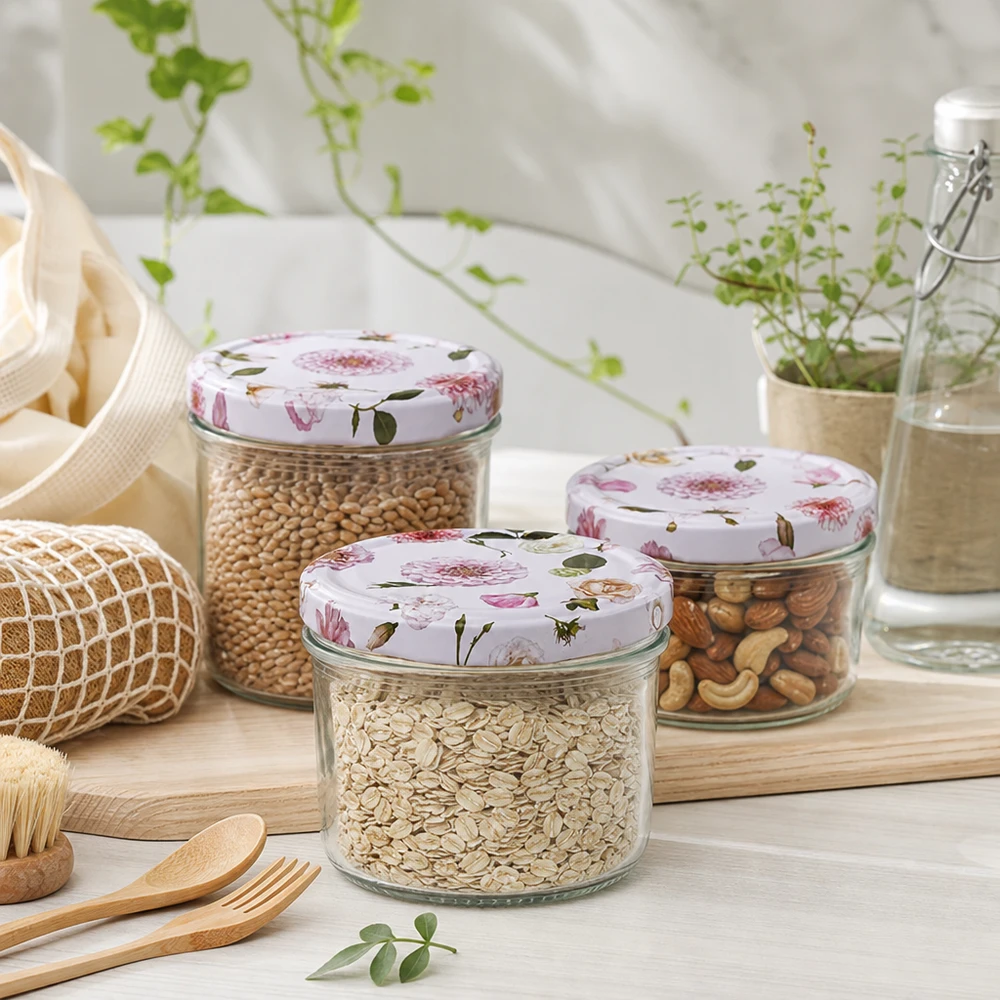 Pot cylindrique de 230 ml + couvercle BasicSeal rose fleur Trois bocaux cylindriques de 230 ml au couvercle rose fleuri remplis de céréales et de noix dans un environnement de cuisine durable