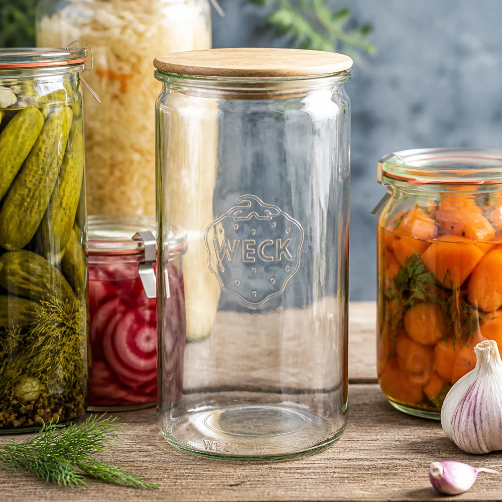 1590ml bocal cylindrique WECK RR100 avec couvercle en bois WECK Zylinderglas 1590ml RR100 mit Holzdeckel zwischen Einmachgläsern mit Gurken Karotten und Sauerkraut auf Holztisch