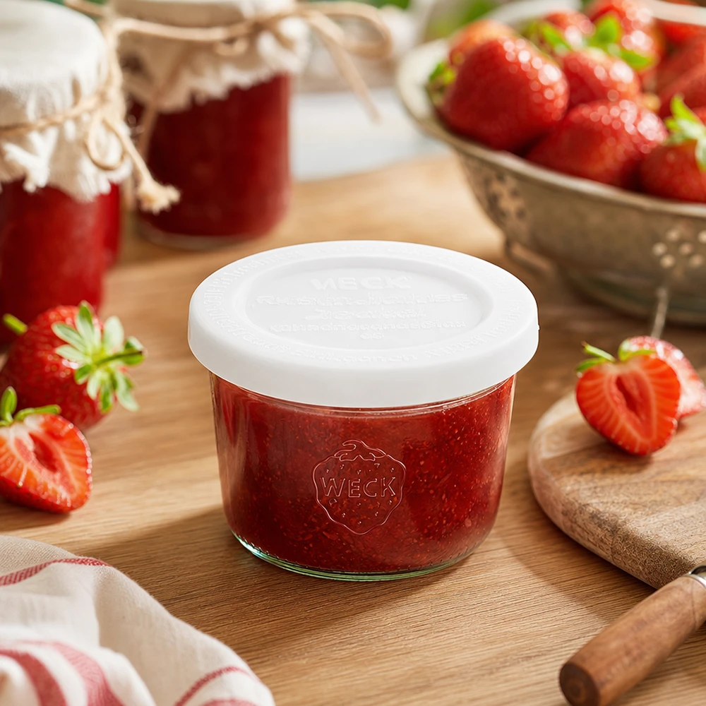 WECK Pot renversé de 80ml RR60 rempli de confiture de fraises sur planche en bois entourée de fraises fraîches et de pots de confiture