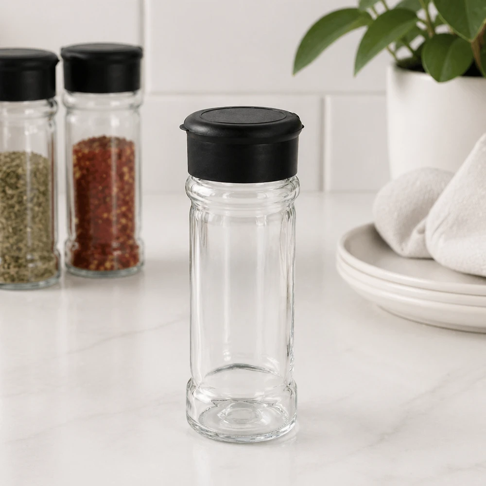 Pot à sel/épices 100 ml avec saupoudreuse, noir Petite salière en verre de 100 ml avec couvercle noir, posée sur un socle en marbre blanc