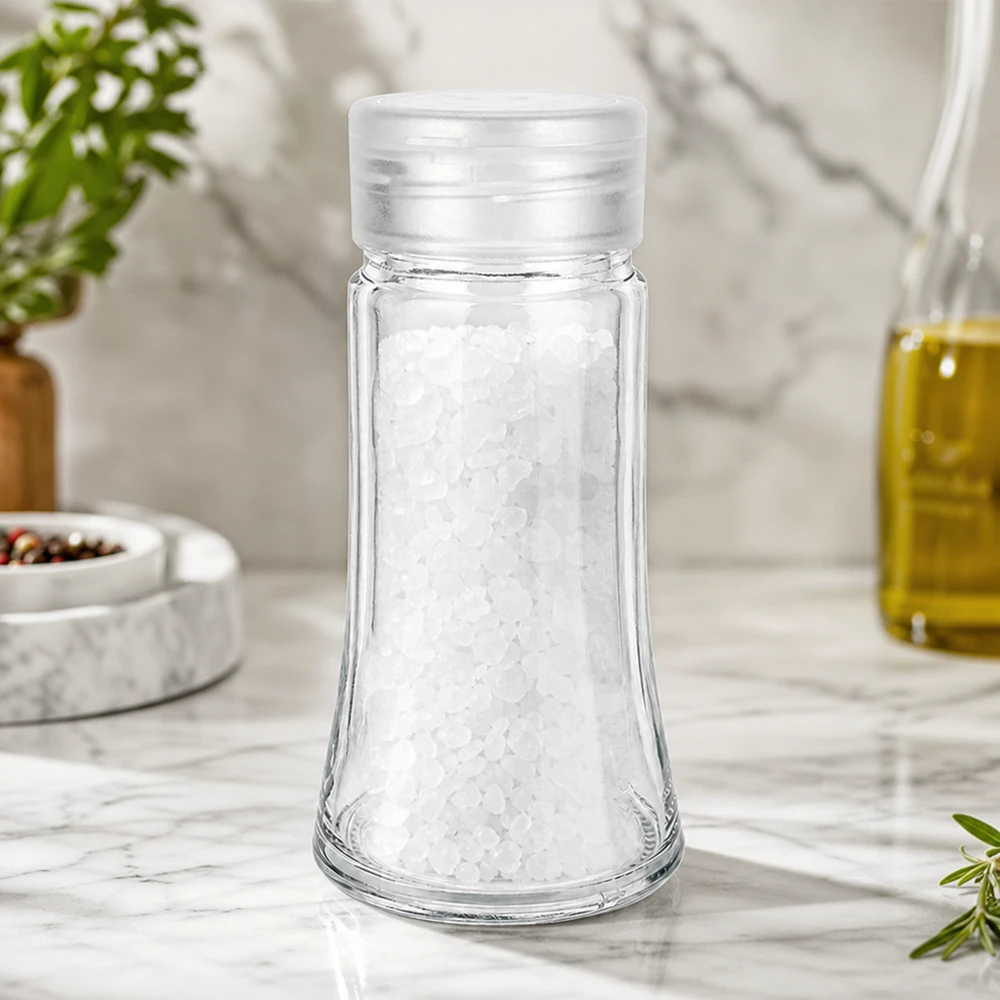 Pot à sel/épices 95 ml avec saupoudreuse, blanc Saupoudreuse en verre de 95 ml remplie de gros sel marin, posée sur un plan de travail en marbre blanc