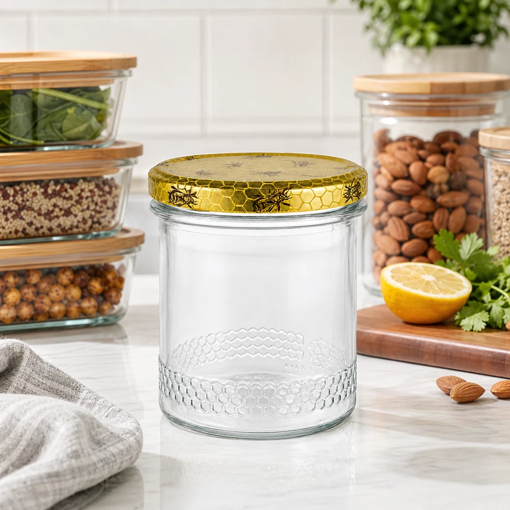 Pot à miel 560 g avec couvercle motif rayon de miel BasicSeal UNiTWIST Pot de miel de 400 ml avec couvercle doré en nid d'abeille sur le plan de travail de la cuisine, bocaux à provisions avec des noix en arrière-plan
